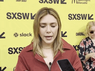 a woman is standing in front of a yellow sign holding a cell phone .