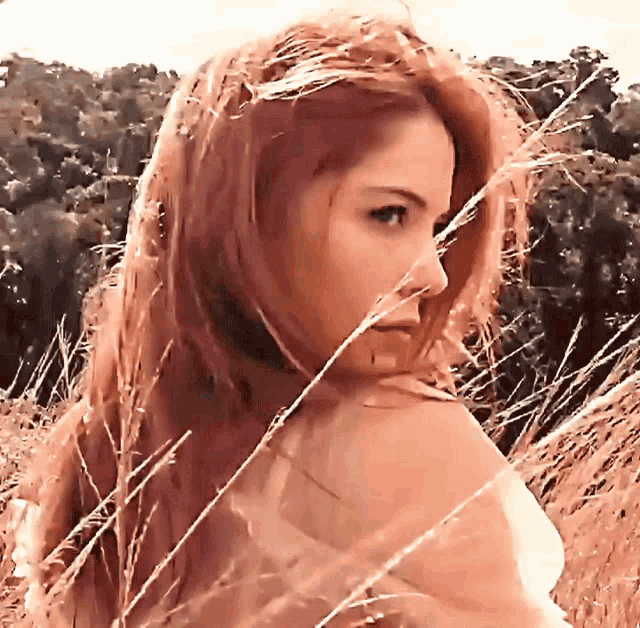 a woman with red hair is standing in tall grass