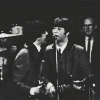 a black and white photo of a man playing a guitar and singing into a microphone on a stage .
