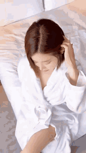 a woman in a white robe is sitting on a bed looking down .