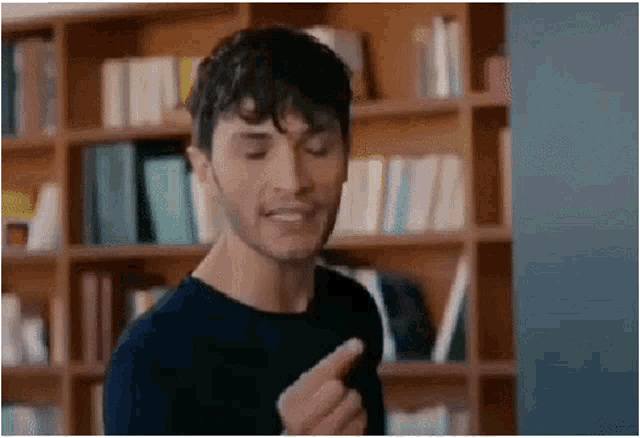 a man in a black shirt is standing in front of a bookshelf in a library .