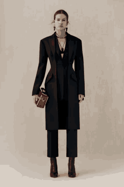 a woman in a black coat and pants is holding a red bag