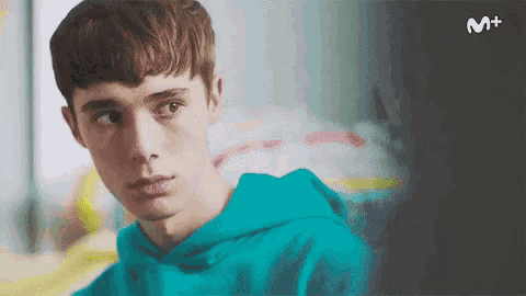 a young man in a blue hoodie is looking at the camera with a m + logo in the background