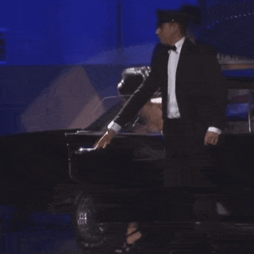 a woman in a black dress is walking on a stage with a car in the background .
