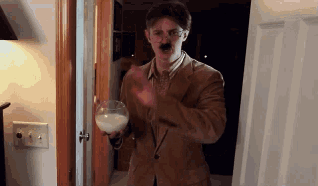 a man with a mustache and glasses holds a glass of milk