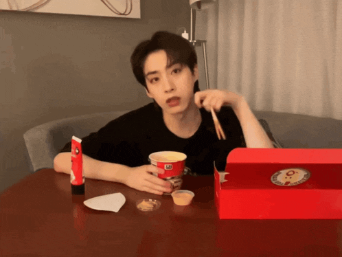 a man sits at a table with a cup of food and a box of food