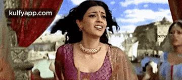 a woman in a purple top and necklace is standing in front of a building .