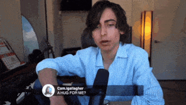 a man in a blue and white striped shirt is talking into a microphone and asking for a hug for him