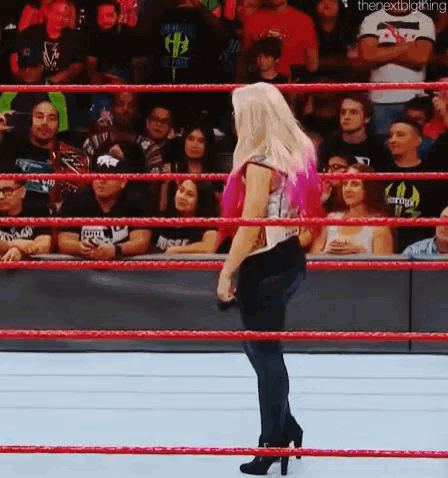 a woman in high heels is standing in a wrestling ring with a crowd watching .