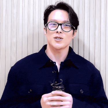 a man wearing glasses and a blue jacket is holding something in his hand