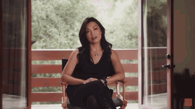 a woman sits in a director 's chair in front of a balcony with the letters bc on the bottom