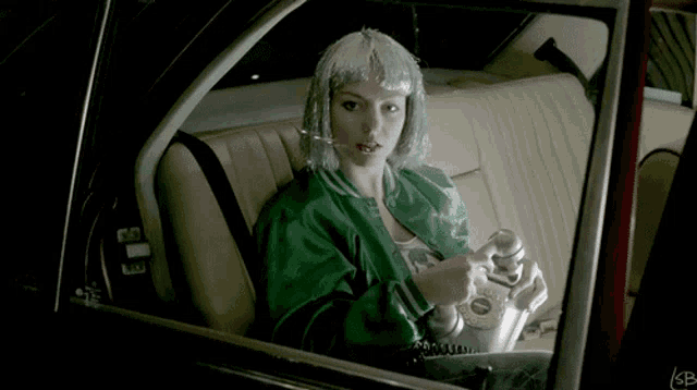 a woman in a green jacket sits in the back seat of a car holding a phone