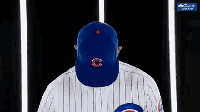 a baseball player wearing a cubs hat is standing in front of a dark background .