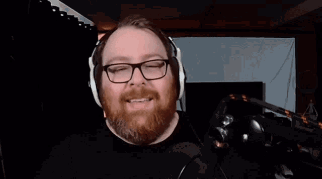 a man with glasses and a beard is wearing headphones and smiling in front of a microphone