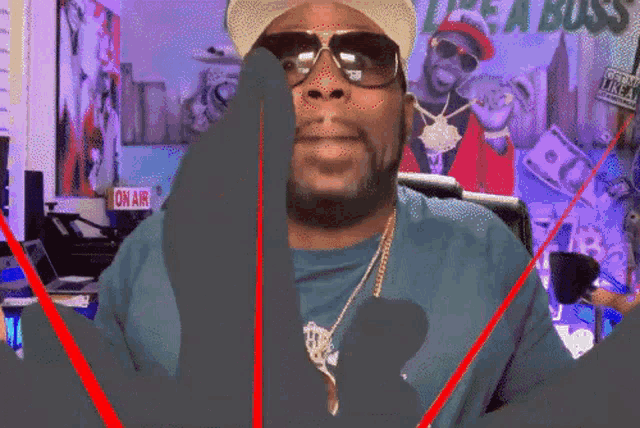 a man wearing sunglasses and a hat stands in front of a sign that says ' on air '
