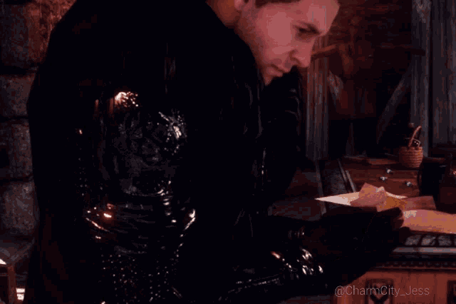 a man in a black jacket is standing in a dark room with the name charmcity jess on the bottom right
