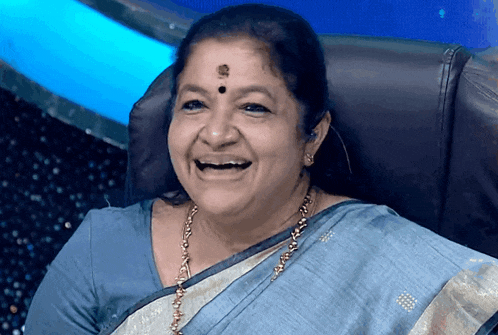 a woman wearing a blue saree and gold necklace is smiling