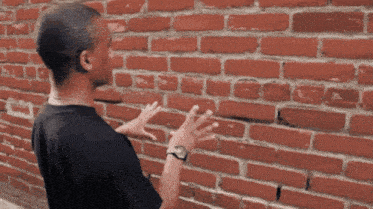 a man wearing a watch is touching a red brick wall