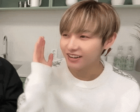 a young man wearing a white sweater is waving his hand