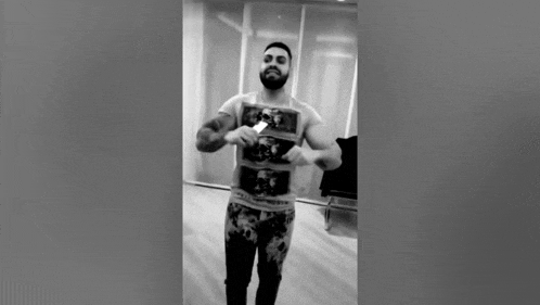 a man with a beard is standing in a room in a black and white photo holding a card .