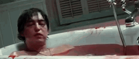 a man is laying in a bloody bathtub with blood coming out of his mouth .