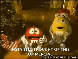 two m & m 's are standing next to each other in front of a christmas tree in a commercial .