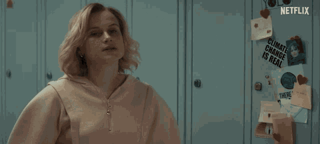 a woman stands in front of a locker with a climate change is real sign on it