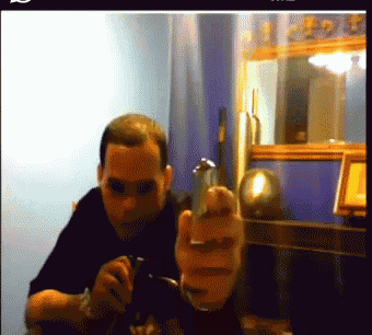 a man is sitting at a table holding a gun and pointing at the camera