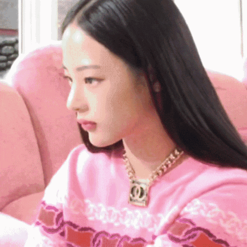 a woman wearing a pink sweater and a necklace with a chanel logo on it