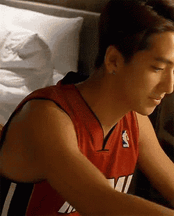 a man in a red nba jersey is sitting on a bed .