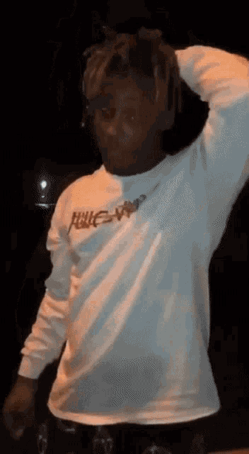 a man wearing a white long sleeve shirt is standing in the dark with his hand on his head .