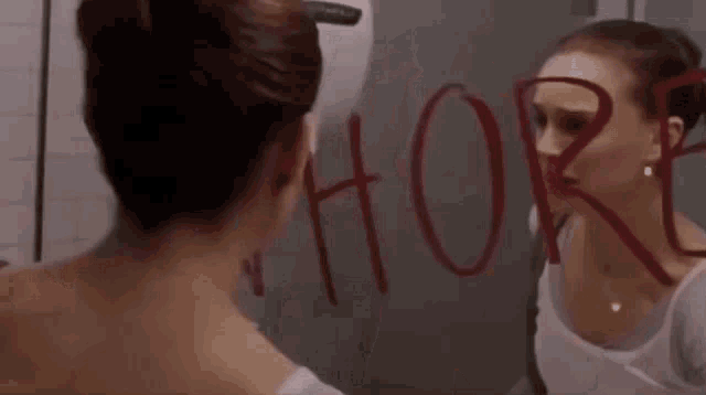 a woman is looking at herself in a bathroom mirror and has the word whore written on the mirror .
