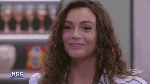 a woman with curly hair is smiling in front of a sign that says #gf on it