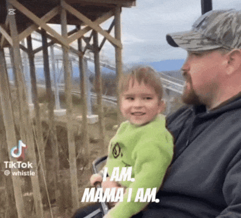 a man is holding a little boy who is wearing a green shirt that says mama i am