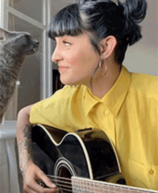 a woman in a yellow shirt is playing a guitar