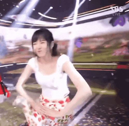 a woman in a white top and a floral skirt is dancing on a stage