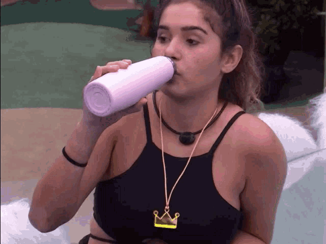 a woman drinking from a pink bottle with a crown necklace