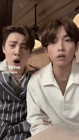 two young men are sitting next to each other with their mouths open and one of them is wearing a striped shirt .