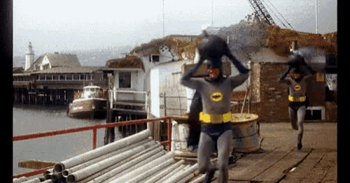 two men in batman costumes are running on a pier