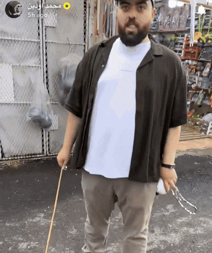 a man with a beard is holding a cane in front of a fence with arabic writing on it
