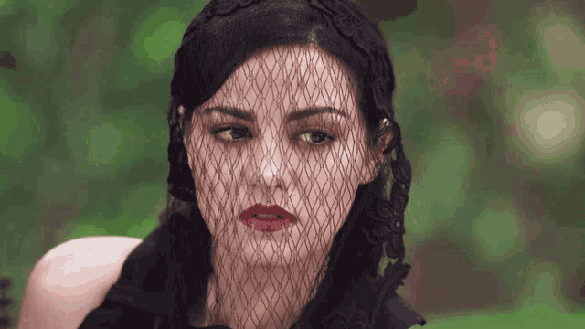 a woman wearing a black dress and veil looks at the camera