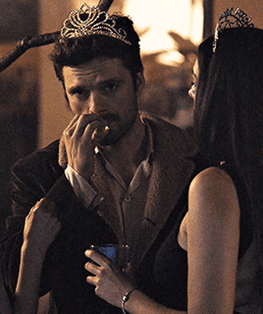 a man with a crown on his head looks at a woman holding a drink