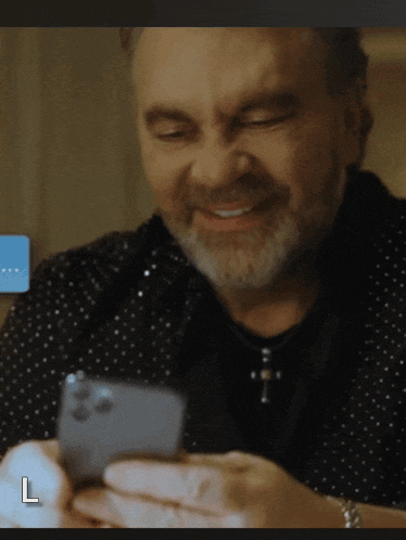 a man with a beard is smiling while looking at his phone with the letter l next to him