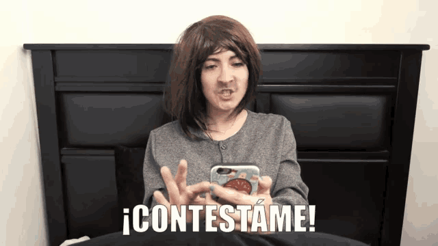 a woman sitting on a bed holding a cell phone with the words contestame above her
