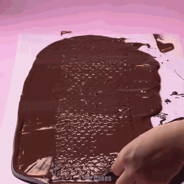 a person is spreading chocolate on a piece of wax paper that says cupcakes on it