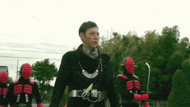 a man in a black sweater is standing in front of a group of red masked people .