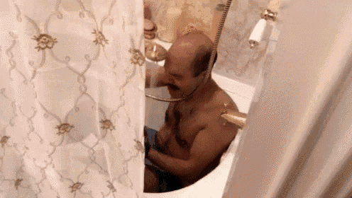 a bald man is taking a bath in a bathtub with a shower curtain behind him .