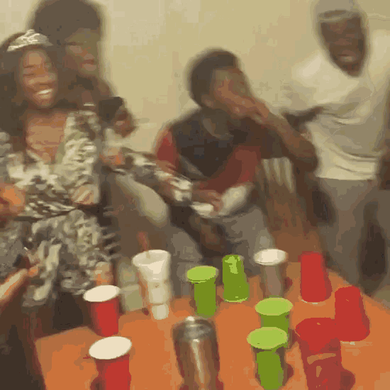 a group of people are sitting around a table with red cups and green cups on it