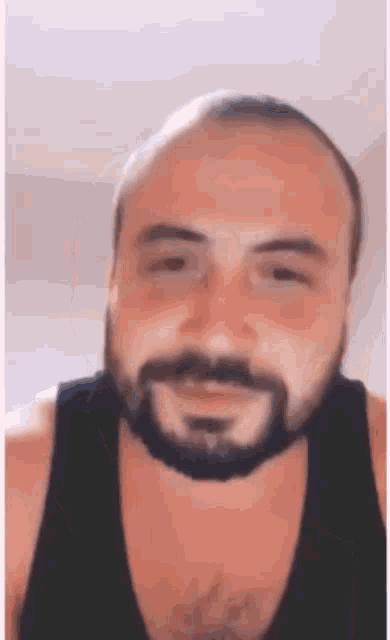 a man with a beard is wearing a black tank top and looking at the camera .