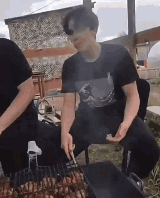 a man in a black shirt is cooking food on a grill